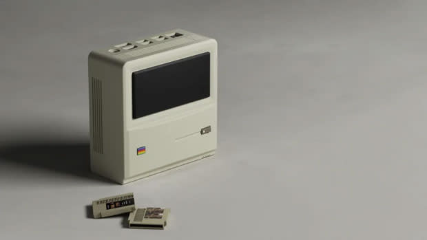 Image of the Ayaneo AM01 Mini PC on a grey table, flipped up on its side so its Apple Mac-inspired design is visible.