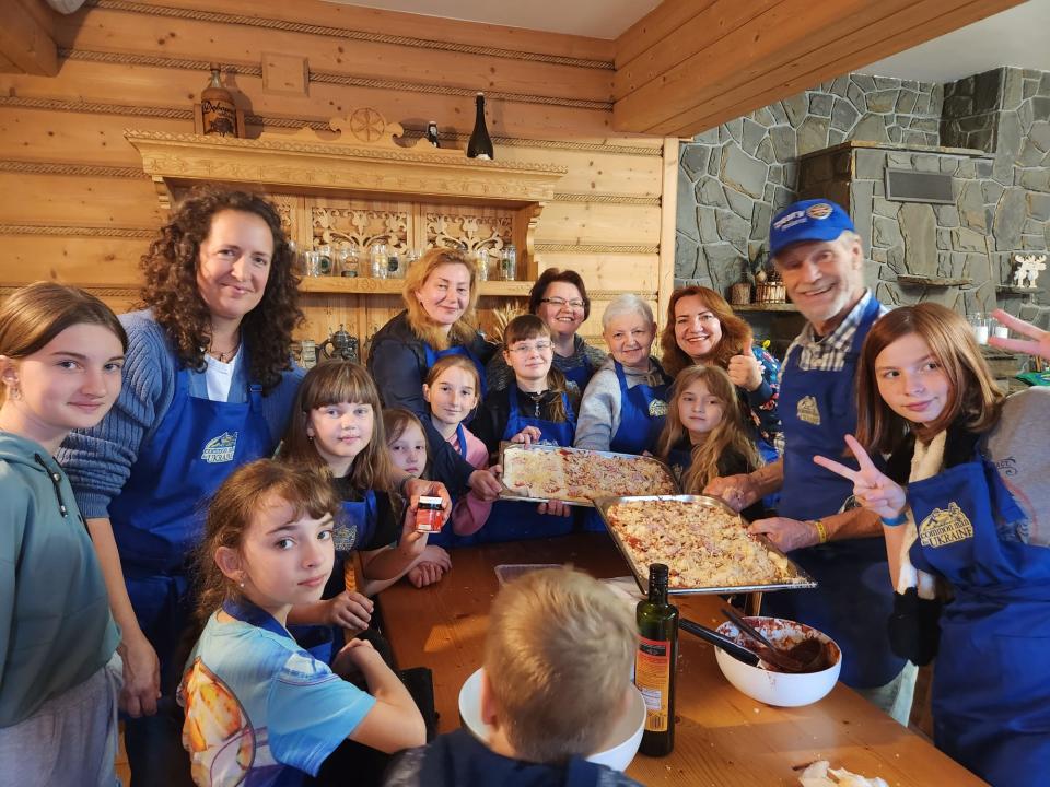 Members of U.S. nonprofit Common Man for Ukraine pose holding homemade pizza with Ukrainian kids during a trauma healing retreat in Zakopane, Poland, in May 2023. The monthly retreats are for kids have lost a loved one during Russia's war in Ukraine.