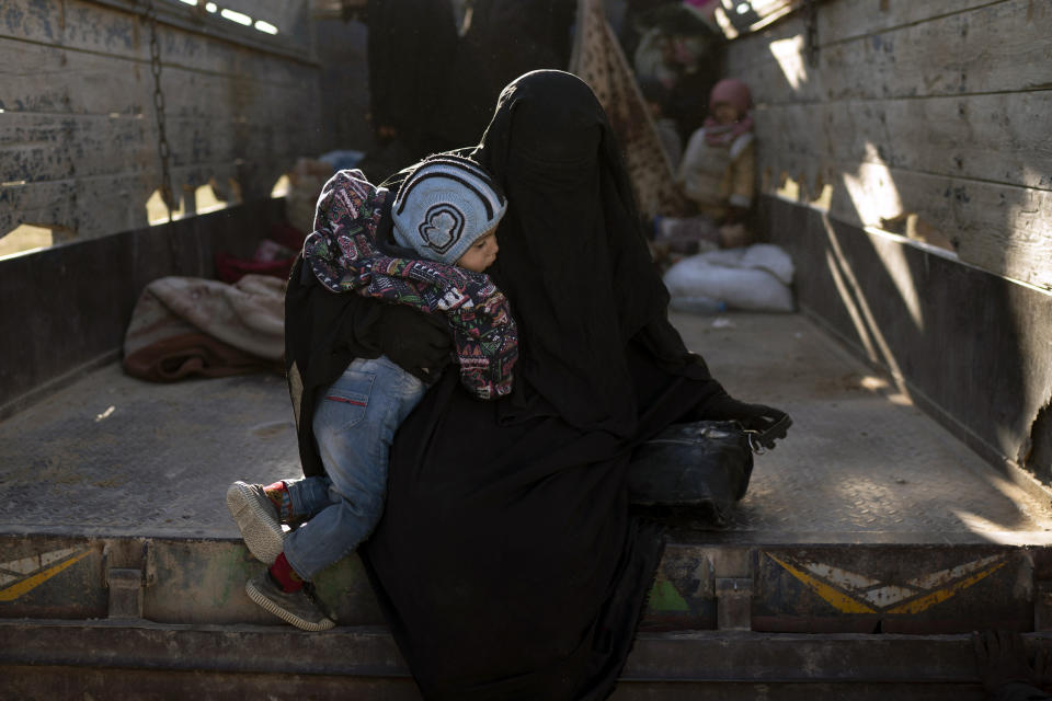 A woman holding a child exits the back of a truck as they arrive to a U.S.-backed Syrian Democratic Forces (SDF) screening area after being evacuated out of the last territory held by Islamic State militants, in the desert outside Baghouz, Syria, Friday, March 1, 2019. (AP Photo/Felipe Dana)