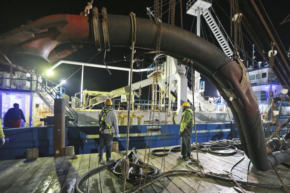 In this Tuesday, Nov. 26, 2019 photo, Workers prepare to attach suction hose to the menhaden fishing boat Windmill Point at Omega Protein's menhaden processing plant on Cockrell's Creek in Reedville, Va. The Trump Administration is threatening to effectively ban a company that makes fish oil pills from fishing in the Chesapeake Bay over mounting concerns from regulators, governors and environmental groups about overfishing. Earlier this year, the company Omega Protein exceeded harvest limits in the bay by more than 30% on a bony and oily fish called Atlantic menhaden. (AP Photo/Steve Helber)