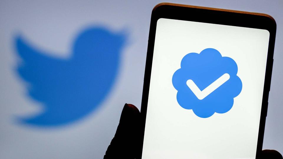 A twitter blue checkmark on a phone screen with the Twitter logo in the background