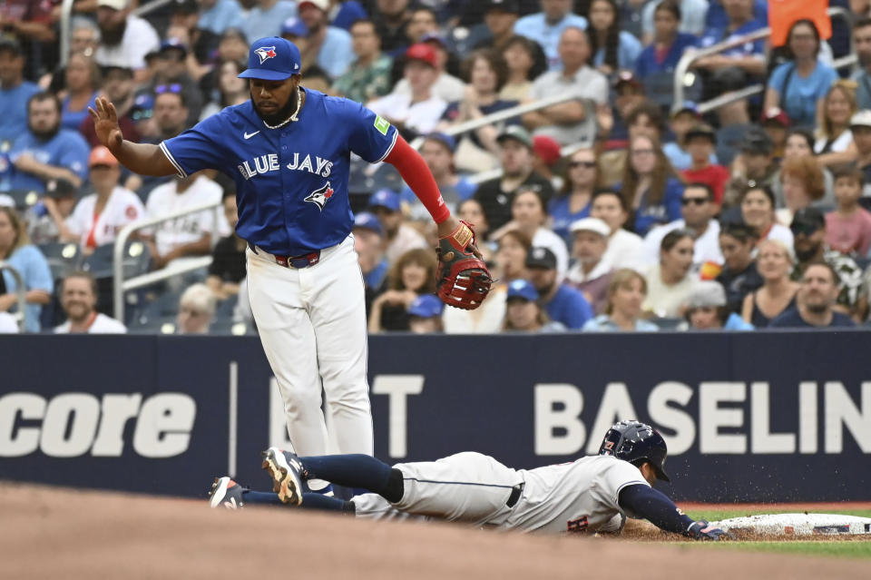 Houston Astros' Jose Altuve (27) dives safely into first base as Toronto Blue Jays first baseman Vladimir Guerrero Jr. (27) looks during the first inning of a baseball game, Tuesday, July 2, 2024, in Toronto. (Jon Blacker/The Canadian Press via AP)