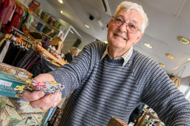 Puzzlemaster Mike Barry who volunteers at Hogs charity shop, Chelsea Road, Bath where one of his jobs is checking jigsaws for missing pieces. See SWNS story SWJIGSAW; A pensioner could be in the running for the world's most tedious job, completing jigsaws puzzles - just to find the missing pieces. Michael Barry, 76, started doing the job two years ago when a new charity shop, Help Us Give Support, opened in his home city. Having done puzzles for the last 40 years of his life, he saw it as a way to help out, being the only thing he is good at, and spends hours every day piecing them together. The retired builder will often sit down on an evening, put on classic FM, puzzling away till the early hours with his rescue cat, Norman.