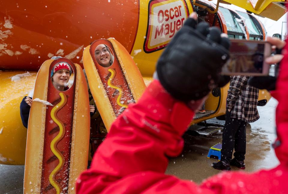 Alex Krawczyk, left, and Faith Schiefer, get their photo taken by Sam Dlott, next to Oscar Mayer's Wienermobile, during a snowy day in Shelby Township on Friday, March 22, 2024.
