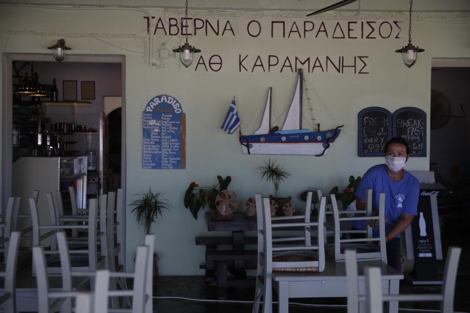 A worker places chairs at a tavern in Plaka beach, on the Aegean island of Naxos, Greece, Wednesday, May 12, 2021. With debts piling up, southern European countries are racing to reopen their tourism services despite delays in rolling out a planned EU-wide travel pass. Greece Friday became the latest country to open up its vacation season as it dismantles lockdown restrictions and focuses its vaccination program on the islands. (AP Photo/Thanassis Stavrakis)