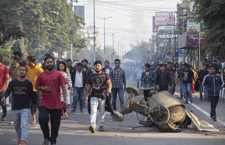 Protestors walk past a cement mixer lies toppled during Wednesday's protest against the Citizenship Amendment Bill (CAB) in Gauhati, India, Thursday, Dec. 12, 2019. Police arrested dozens of people and enforced curfew on Thursday in several districts in India’s northeastern Assam state where thousands protested legislation granting citizenship to non-Muslims who migrated from neighboring countries. (AP Photo/Anupam Nath)