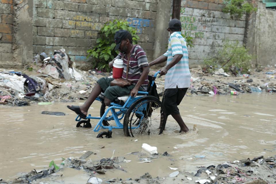 Un hombre en silla de ruedas recibe ayuda para cruzar una calle anegada por las fuertes lluvias, en Puerto Príncipe, Haití, el 3 de junio de 2023. (AP Foto/Odelyn Joseph)