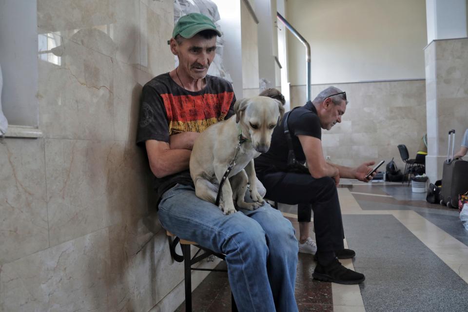 man in baseball hat and blue jeans sits with a dog in his lap waiting