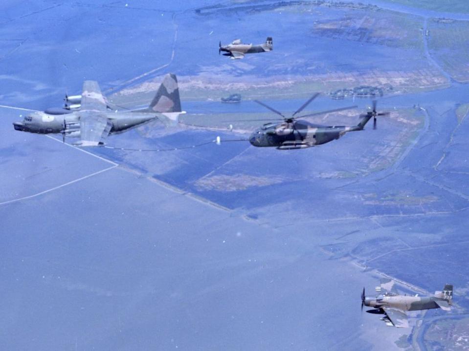 Two US Air Force Douglas A-1H Skyraiders flying in formation as a HH-53C helicopter refuels a US Air Force HC-130P in the skies above Southeast Asia.