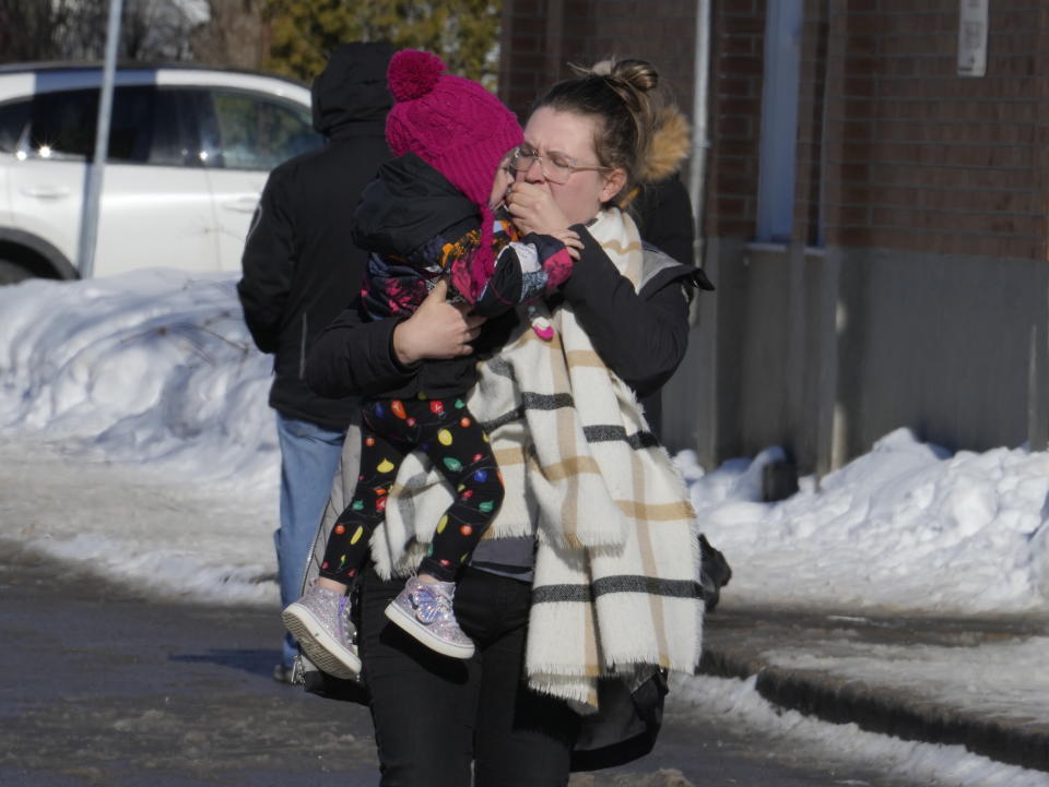 A woman carries a child from a daycare centre after a city bus crashed into the facility in Laval, Quebec, Wednesday, Feb.8, 2023. At least eight people including several children have been sent urgently to hospital after a city bus crashed into a daycare north of Montreal Wednesday morning, emergency officials say. (Ryan Remiorz/The Canadian Press via AP)