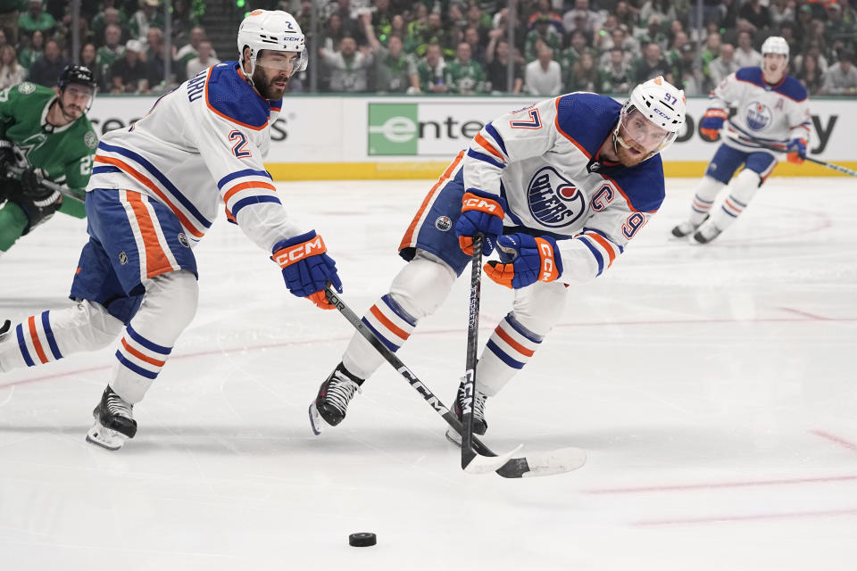 Edmonton Oilers defenseman Evan Bouchard (2) and center Connor McDavid (97) work to take control of the puck during the first period in Game 2 of the Western Conference finals in the NHL hockey Stanley Cup playoffs against the Dallas Stars, Saturday, May 25, 2024, in Dallas. (AP Photo/Tony Gutierrez)