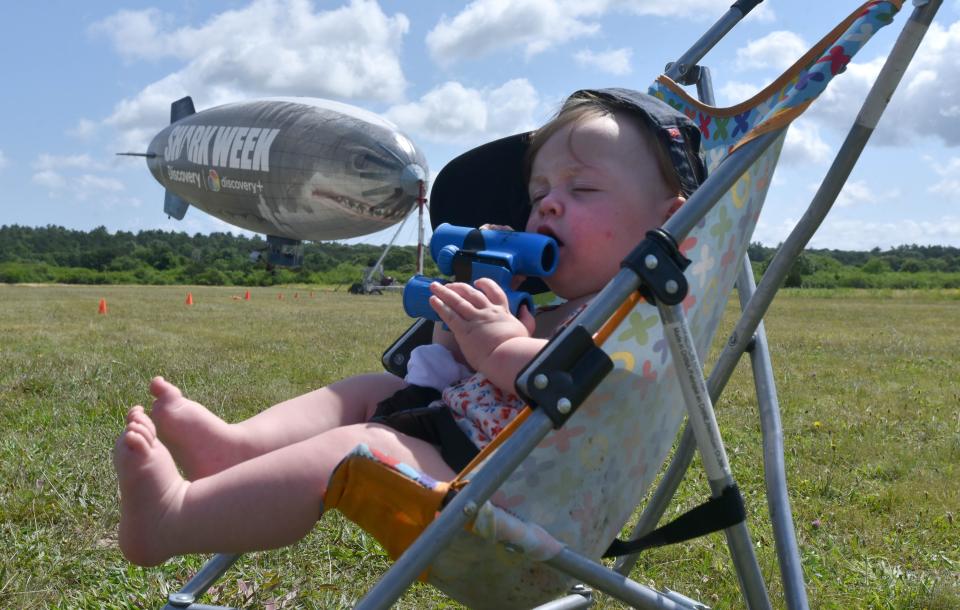 MARSTONS MILLS 07/12/22 Eight month old Emery Oberg  pays no mind to the nearby shark, sleeping with the binoculars as a 130 foot blimp promoting the Discovery Channel's Shark week drifts in the wind at the Cape Cod Airfield in Marstons Mills. Steve Heaslip/Cape Cod Times 