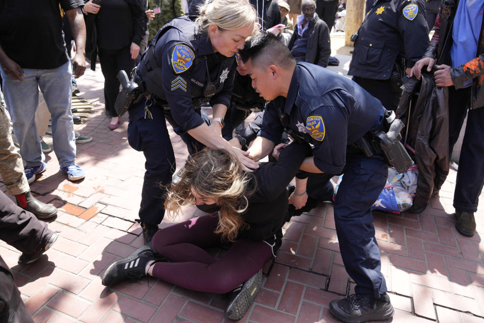 A protester who threw a brick at a color guard after a rare outdoor meeting of the Board of Supervisors is restrained by police at UN Plaza in San Francisco, Tuesday, May 23, 2023. Mayor London Breed attempted to answer questions from supervisors demanding her administration do more to shut down open-air drug dealing, but the meeting had to be moved indoors to City Hall because of disruptions. (AP Photo/Eric Risberg)