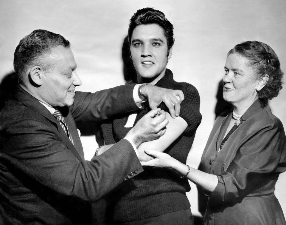 Elvis Presley receives a polio vaccination from Dr. Leona Baumgartner and Dr. Harold Fuerst at CBS studio 50 in New York City.  