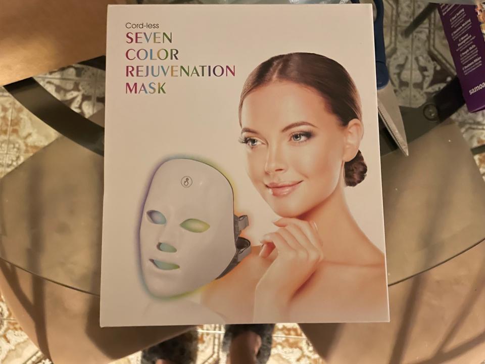 A white box has a brown haired woman next to a whole-face mask with LED lights.