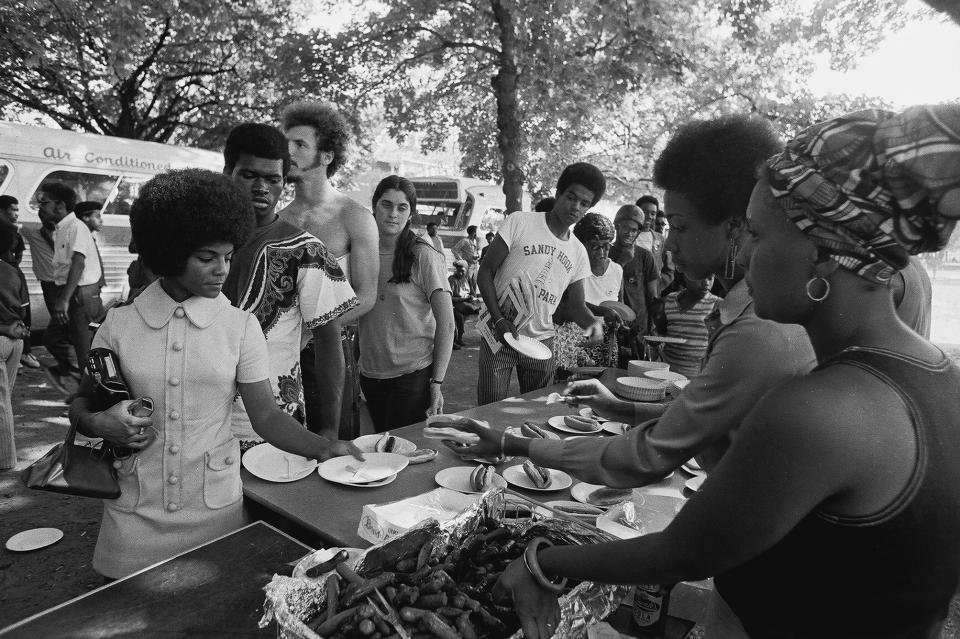Members of the Black Panther Party stand behind tables and distribute free hot dogs to the public in New Haven, Connecticut in the late 1960s.&nbsp;