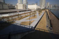 Security guards, bottom right, pass by each other as they patrol the closed area of the riverbank adjacent to a closed building complex, back left, built to be used for the athletes' village during the rescheduled Tokyo Olympics, in Tokyo on Thursday, Jan. 21, 2021. The postponed Tokyo Olympics are to open in just six months. Local organizers and the International Olympic Committee say they will go ahead on July 23. But it’s still unclear how this will happen with virus cases surging in Tokyo and elsewhere around the globe. (AP Photo/Hiro Komae)