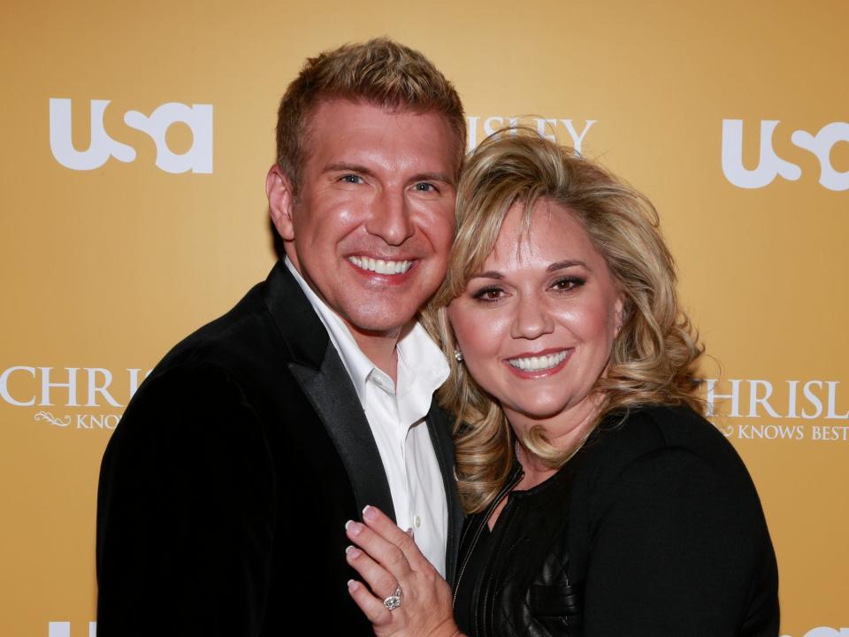 todd chrisley and julie chrisley in front of a yellow USA today sign with her hand on his chest