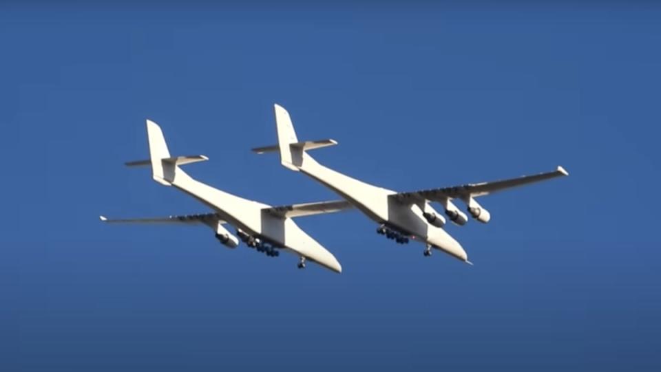 The Roc, the world's largest plane, which looks like a biplane with six engines, flying against a blue sky