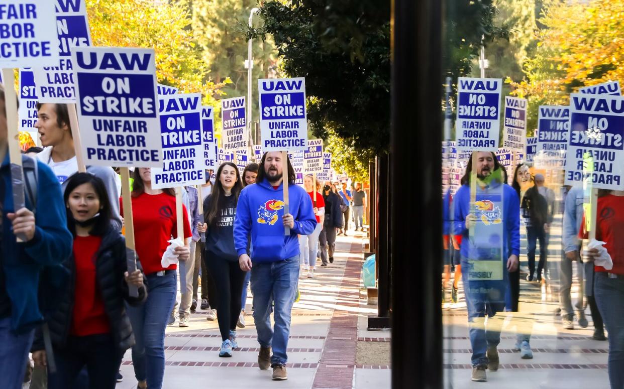 Demonstrators are seen reflected in a window as they picket with signs at UCLA.