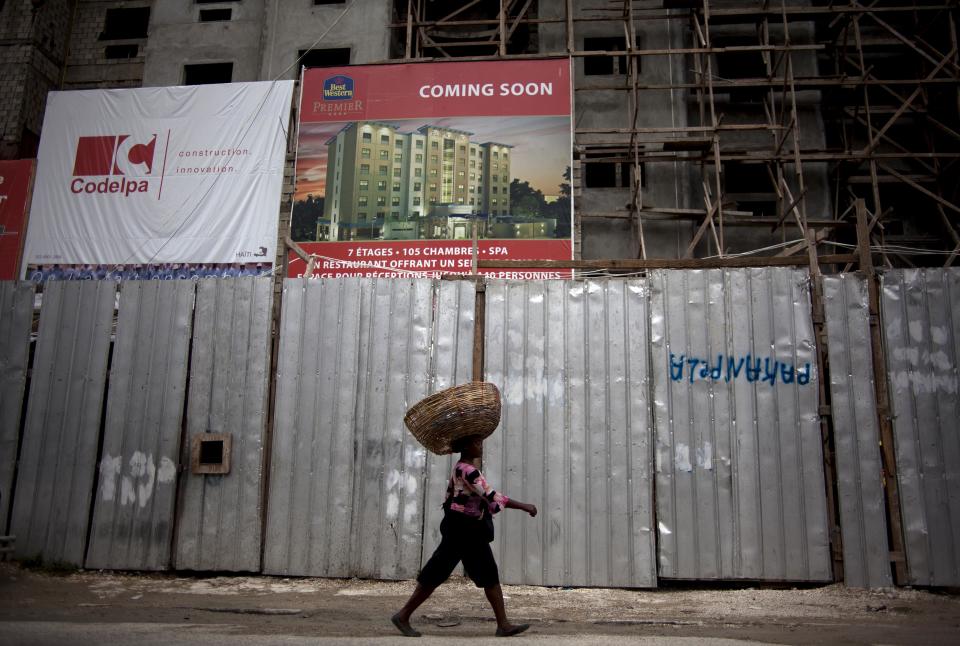 In this Thursday, April 26, 2012 photo, a street vendor walks in front of the building in construction of Best Western Hotel in Port-au-Prince, Haiti. This city is undergoing the largest hotel building boom in its history, raising expectations that investors will soon fill those air-conditioned rooms looking to build factories, tourist infrastructure and other amenities that will help Haiti bounce back from the 2010 earthquake that killed hundreds of thousands of people. (AP Photo/Ramon Espinosa)