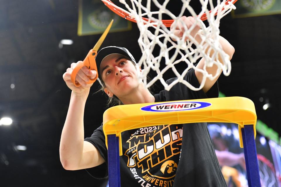 caitlin clark standing on a ladder cutting down a basketball net with scissors