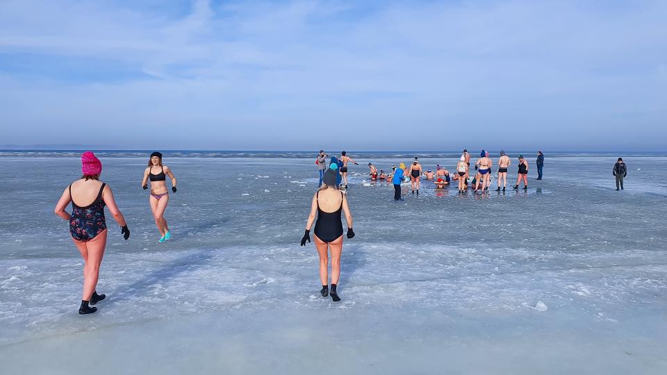 Winter swimming. People winter bathing in the sea. A large group of people is walking on frozen water.