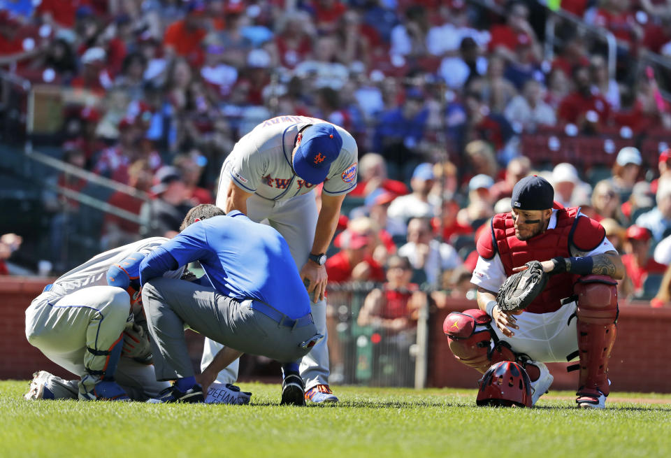 New York Mets' Robinson Cano, left, is checked on by a trainer and manager Mickey Callaway as St. Louis Cardinals catcher Yadier Molina, right, after being injured while batting during the seventh inning of a baseball game Sunday, April 21, 2019, in St. Louis. (AP Photo/Jeff Roberson)