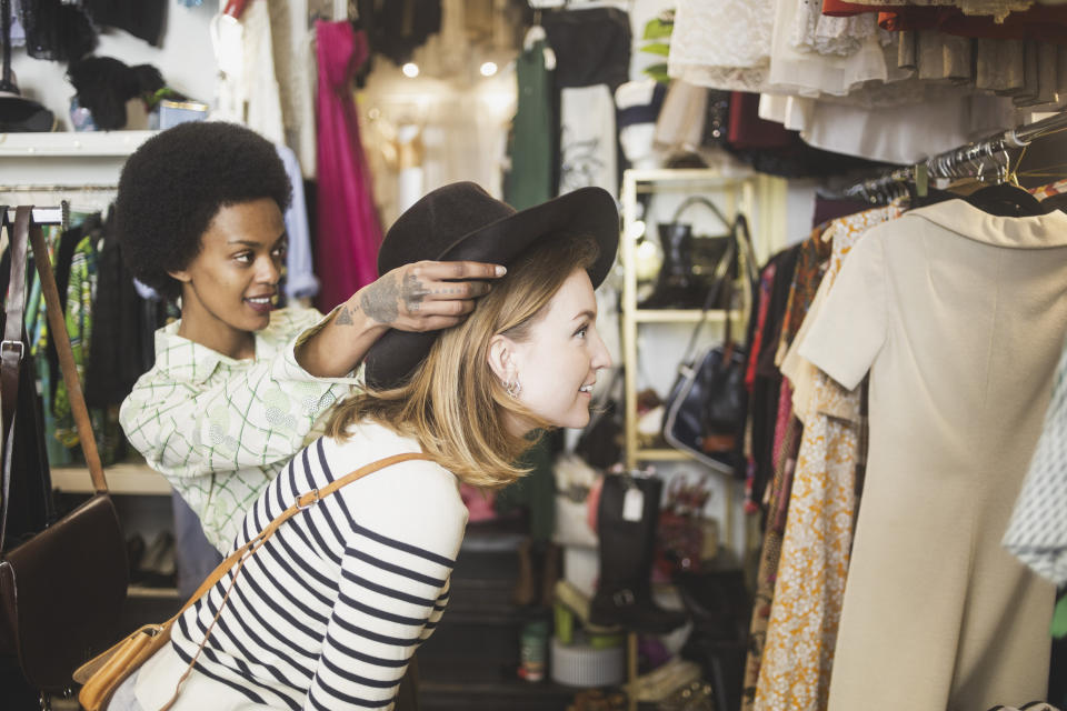 a woman helping another woman put on a hat inside a store