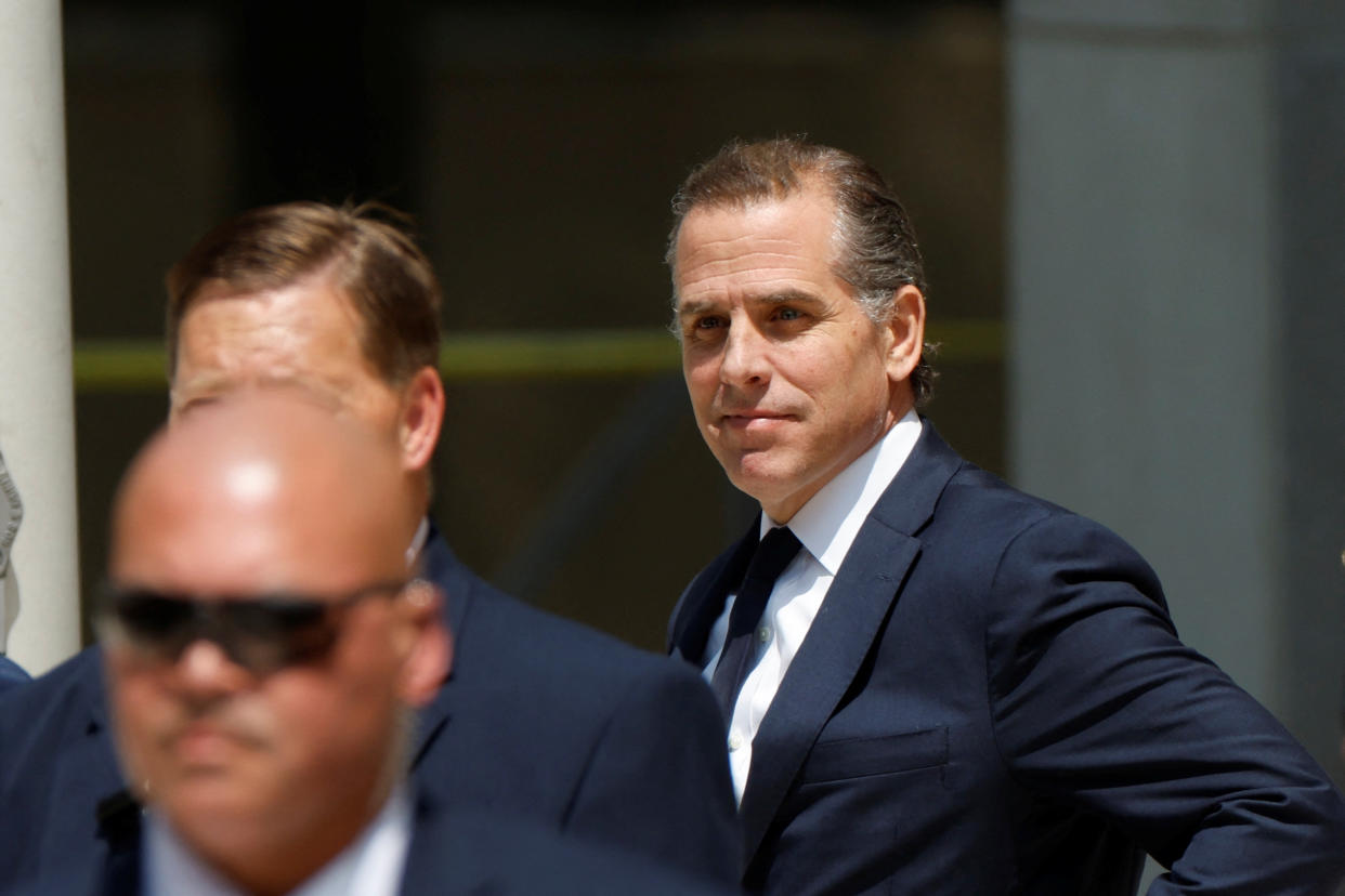Hunter Biden, dressed for court, wears a wry expression outside the courthouse door.