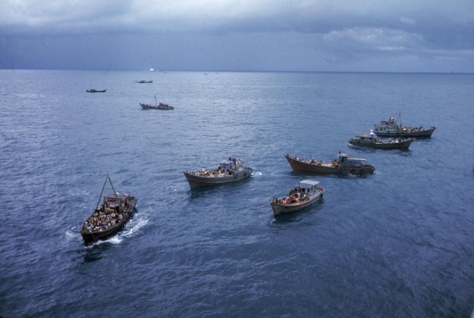 A photo of six boats filled with refugees in the open waters of the South China Sea.