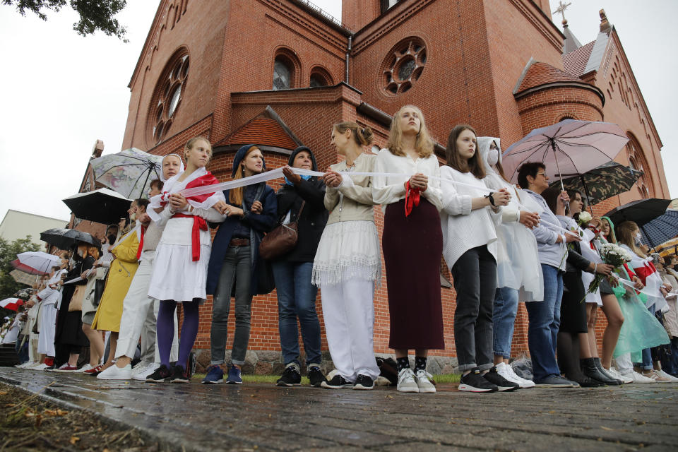 Protesters holding a wait ribbon, a symbol of protest, stand in front of the Church of Saints Simon and Helena during a rally in Minsk, Belarus, Thursday, Aug. 27, 2020. Russian President Vladimir Putin warned that he stands ready to send police to Belarus if protests there turn violent, but added in an interview broadcast Thursday that there is no such need now and voiced hope for stabilizing the situation in the neighboring country. (AP Photo/Dmitri Lovetsky)