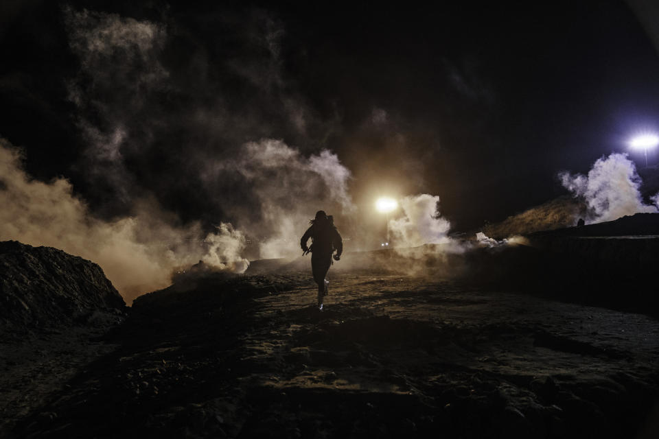 Migrants run as tear gas is thrown by U.S. Border Protection officers to the Mexican side of the border fence after they climbed the fence to get to San Diego, Calif., from Tijuana, Mexico, Tuesday, Jan. 1, 2019. Discouraged by the long wait to apply for asylum through official ports of entry, many migrants from recent caravans are choosing to cross the U.S. border wall and hand themselves in to border patrol agents. (AP Photo/Daniel Ochoa de Olza)