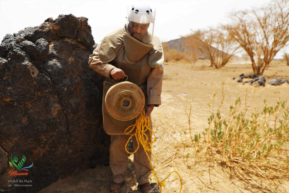 In this undated photograph released Aug. 19, 2018 by the state-run Emirates News Agency (WAM) on behalf of the Saudi-funded Masam anti-mine operation, an unidentified de-miner holds a deactivated mine near Marib, Yemen. Land mines scattered by Yemen’s Houthi rebels will remain a threat even if the latest negotiations succeed in halting the civil war. While the Houthis’ firing of ballistic missiles deep into Saudi Arabia has drawn the most attention, their widespread use of mines within Yemen represents a risk for generations to come in the Arab world’s poorest country. Yemen is also littered with unexploded cluster munitions and bombs dropped by the Saudi-led coalition, including some made in the United States. (WAM via AP)