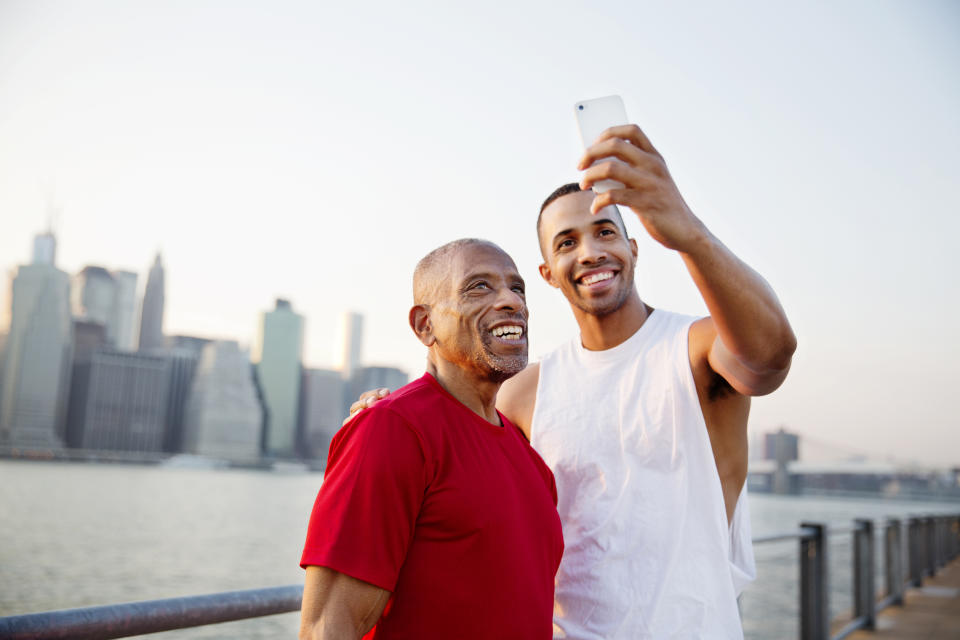 A tall man taking selfie with his father, who is not as tall, by the East River in New York City. 