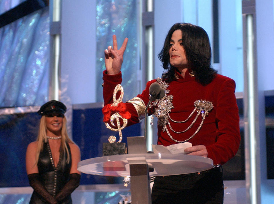 Michael at the podium giving the peace sign with Britney standing behind him