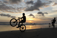 Boys play with their bicycles during sunset on Kuta beach in Bali, Indonesia, Friday, July 10, 2020. Indonesia's resort island of Bali reopened after a three-month virus lockdown Thursday, allowing local people and stranded foreign tourists to resume public activities before foreign arrivals resume in September. (AP Photo/Firdia Lisnawati)