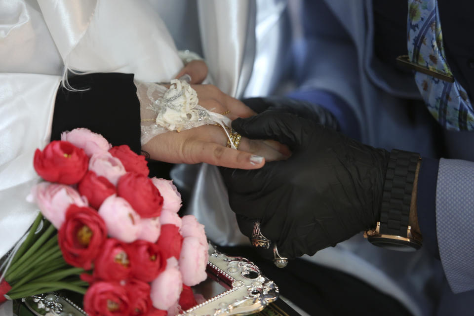 In this Thursday, April 9, 2020 photo, Ahmed Khaled al-Kaabi and his bride Ruqaya Rahim hold hands during their wedding in Najaf, Iraq, the hardest hit town by coronavirus in the country with government banned large public gatherings. Unwilling to postpone the wedding, al-Kaabi asked the local security forces to help him wed his beloved. The police responded by providing the groom vehicles blasting music to bring his bride to the family home for a small celebration of just six people. (AP Photo/Anmar Khalil)