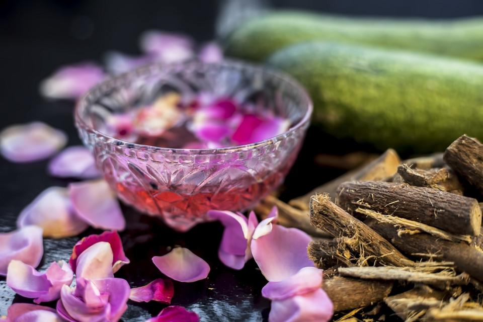 Skin whitening DIY face mask on a black shiny surface consisting of cucumber slices rose water and some mulethi or licorice powder. Shot of rose water, cucumber, and some licorice with its powder.