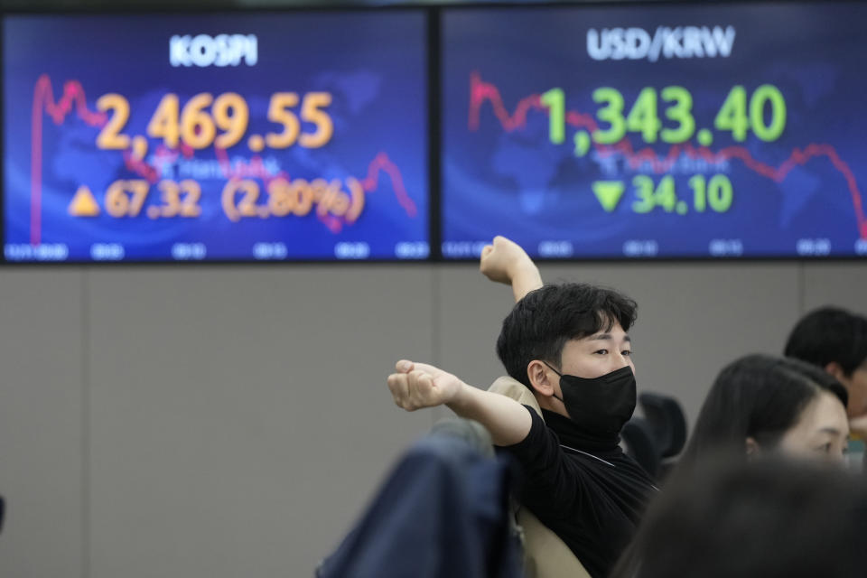 A currency trader stretches near screens showing the Korea Composite Stock Price Index (KOSPI), left, and the exchange rate of South Korean won against the U.S. dollar, at the foreign exchange dealing room of the KEB Hana Bank headquarters in Seoul, South Korea, Friday, Nov. 11, 2022. Asian stock markets surged Friday after U.S. inflation eased by more than expected, spurring hopes the Federal Reserve might scale down plans for more interest rate hikes. (AP Photo/Ahn Young-joon)