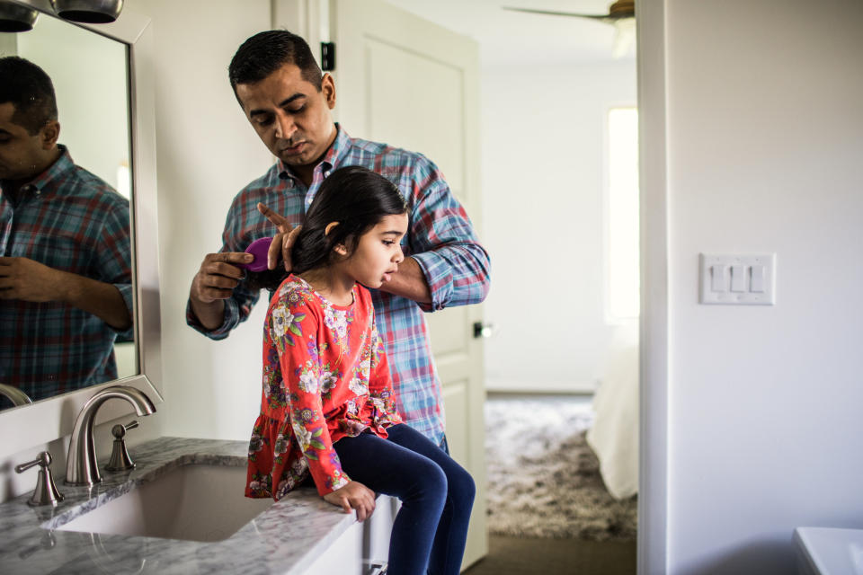 A father fixes his daughter's hair in the bathroom.