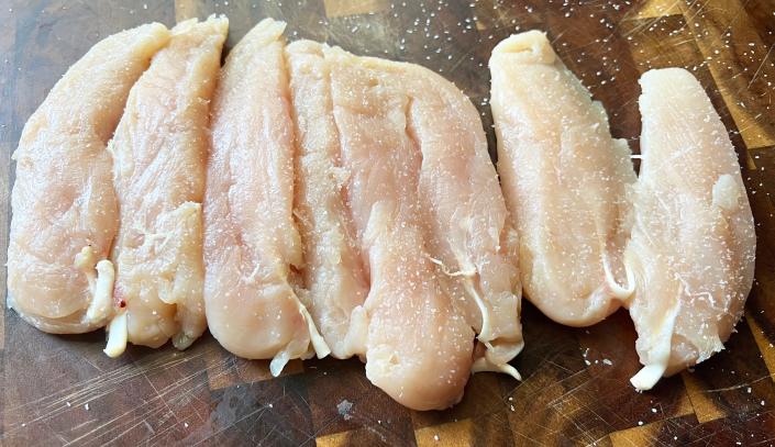 Chicken breast lined up on wooden cutting board