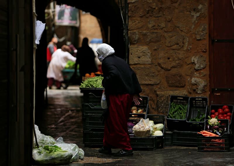 A woman wearing a face mask walks past vegetables and fruit displayed for sale in Sidon