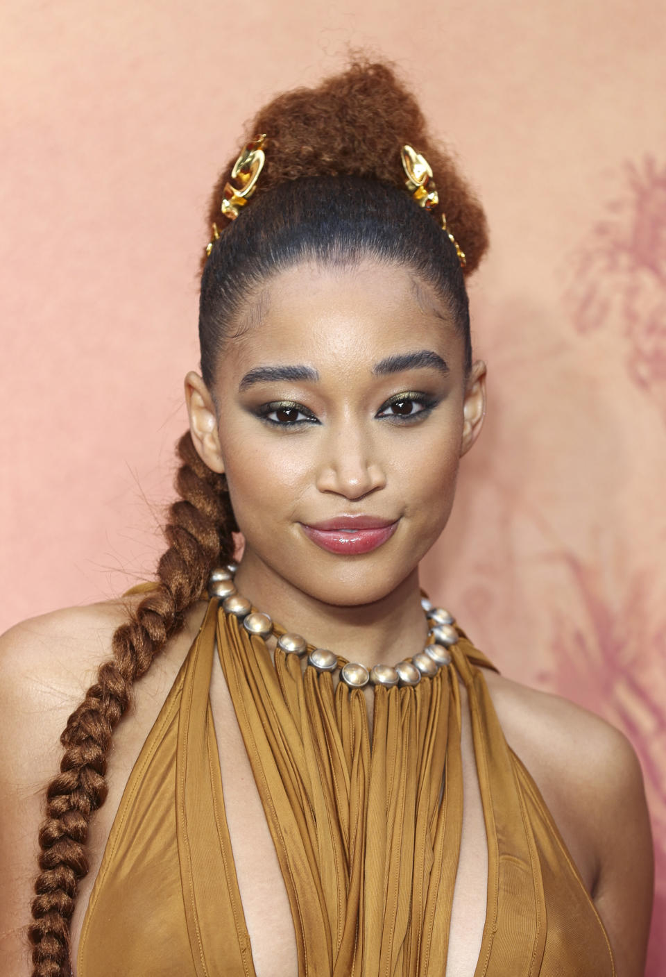 Amandla Stenberg poses with an intricate braided hairstyle and a halter-neck dress, featuring a necklace accent. She is attending an event