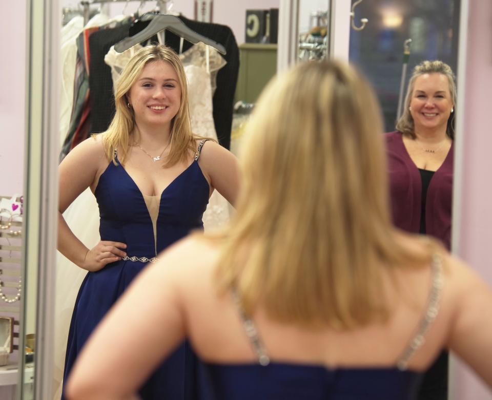 Zoe Leneweaver, 17, of Bridgewater, tries on a deep blue ball gown from Miss Louise Prom Closet and takes a look in the mirror on Thursday, Jan. 13, 2022. Owner Julie Costa, right, approves.