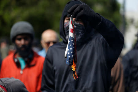 A demonstrator against U.S. President Donald Trump burns an American flag during a rally in Berkeley, California in Berkeley, California, U.S., April 15, 2017. REUTERS/Stephen Lam