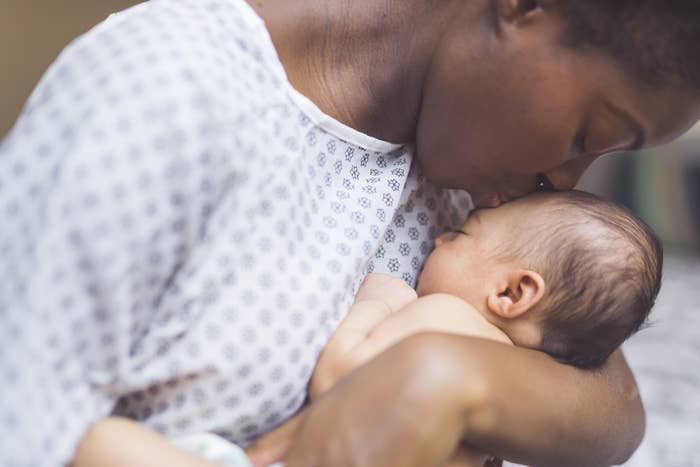 A mother gently kisses her baby's forehead, both in casual attire, sharing a tender moment