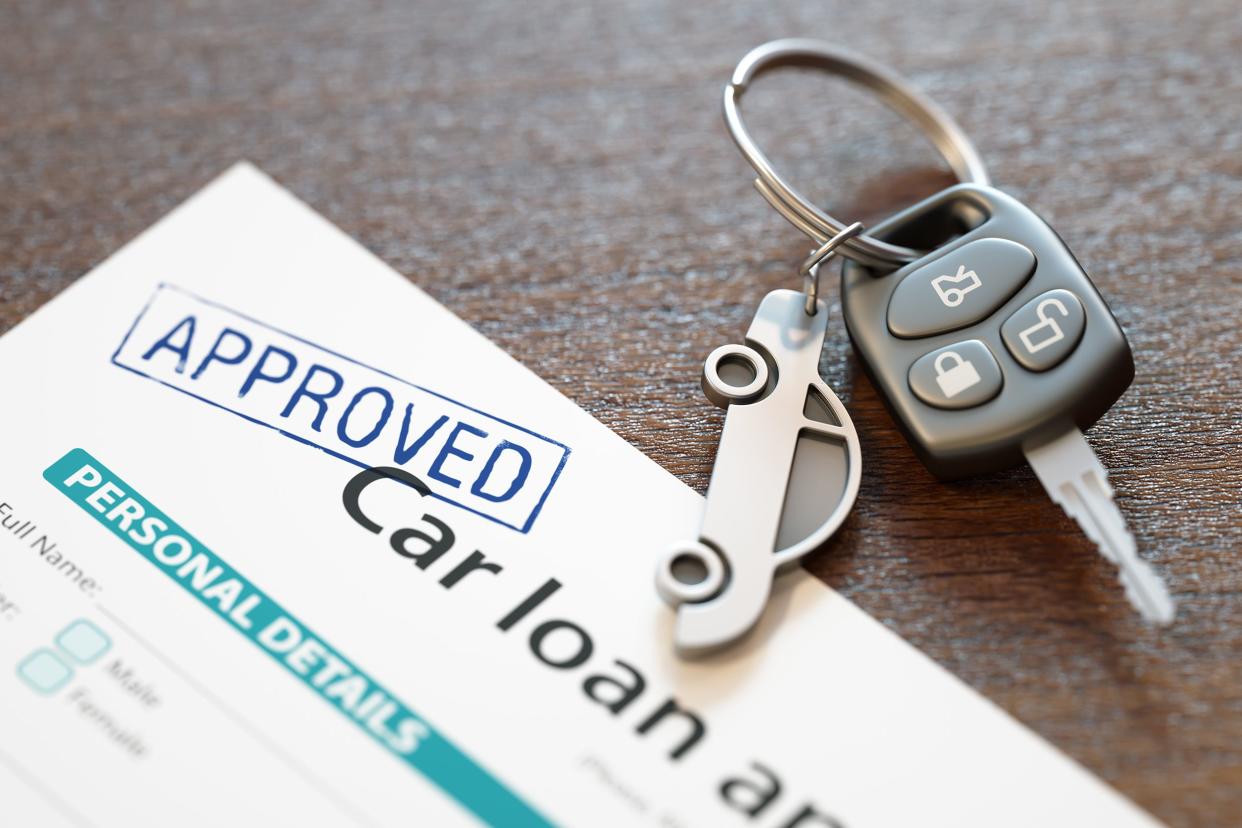 Closeup of car loan application stamped with 'Approved' with car keys on grey table
