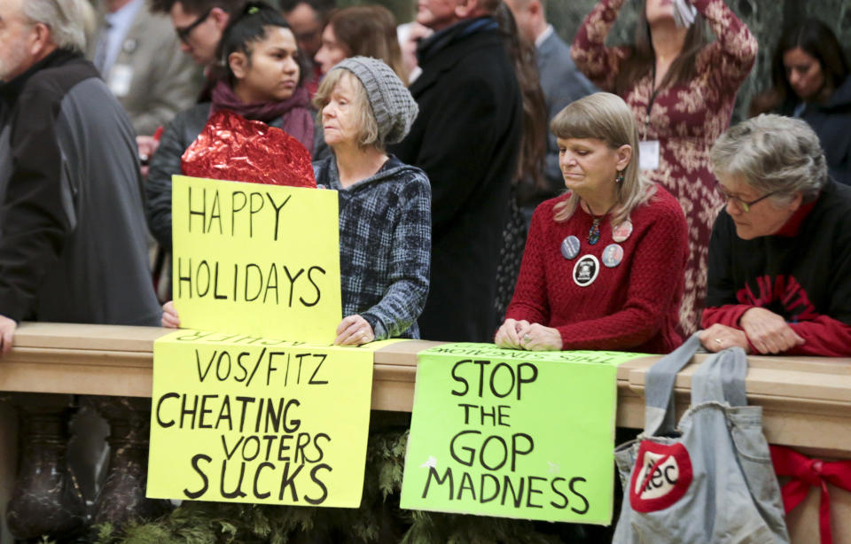 Protesters Peppi Elder, left, and Christine Taylor holds up signs during the state Christmas Tree lighting ceremony in state Capitol Rotunda Tuesday Dec. 4, 2018, in Madison, Wis. The Senate and Assembly are set to send dozens of changes in state law to Gov. Scott Walker's desk. (Steve Apps
