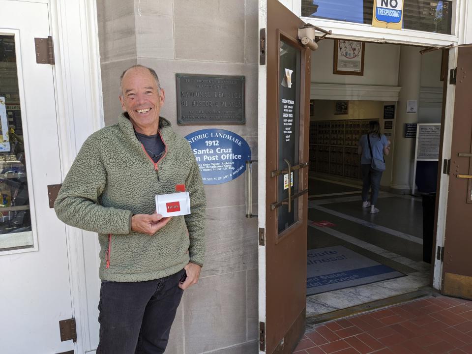 Netflix co-founder or original CEO Marc Randolph stands outside the Santa Cruz, California post office where in 1997 he mailed a Patsy Cline CD to determine whether a disc could make it through the Postal System without being damaged, May 31, 2022 in Santa Cruz, Calif. He is holding a small mailbox that Netflix made in its early days to promote the DVD-by-mail rental service. (AP Photo/Michael Liedtke)